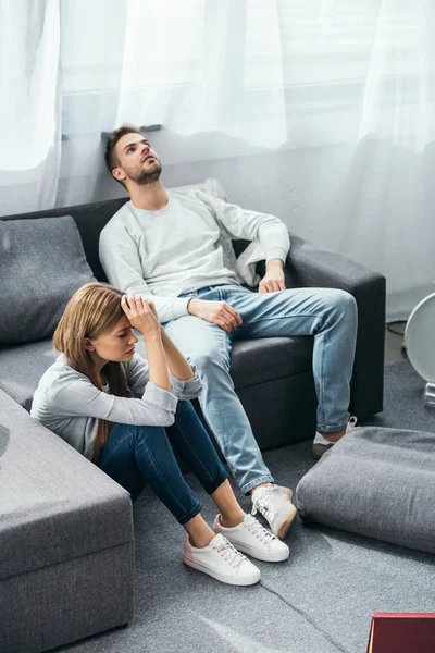 Triste mulher sentada no chão e bonito homem sentado no sofá em apartamento roubado — Fotografia de Stock