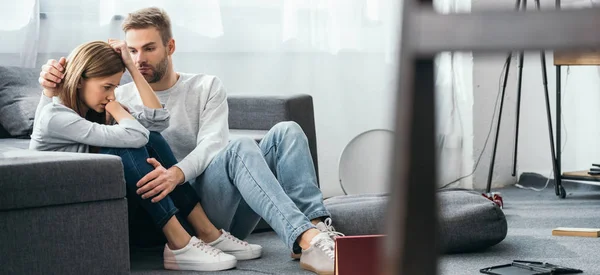 Panoramic shot of handsome man calming down sad woman in robbed apartment — Stock Photo