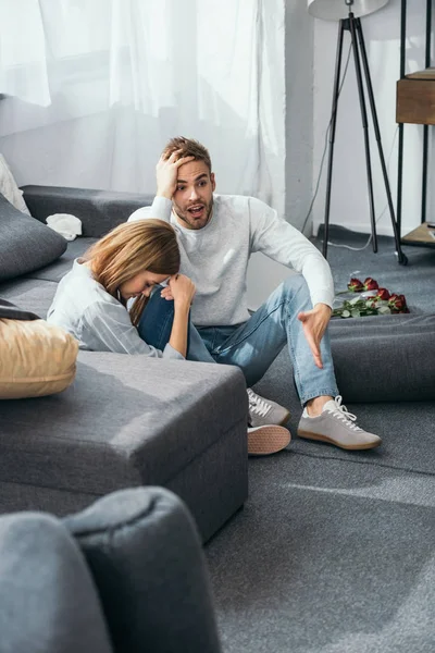 Traurige Frau und schockierter Mann sitzen in beraubter Wohnung auf dem Boden — Stockfoto