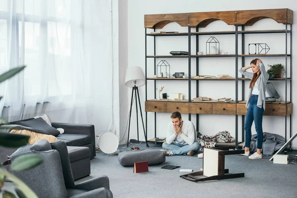 Mujer triste y hombre guapo sentado en el piso en el apartamento robado - foto de stock