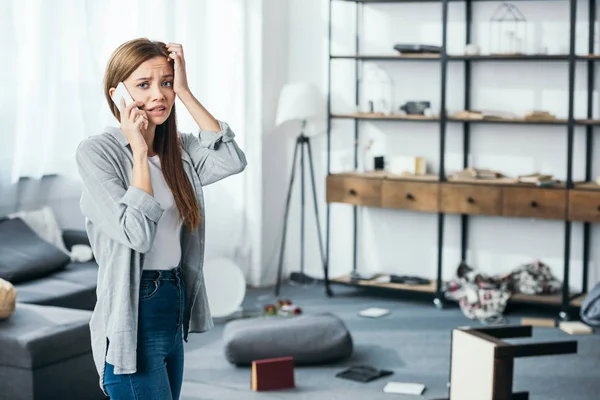 Mujer atractiva y triste hablando en el teléfono inteligente en el apartamento robado - foto de stock