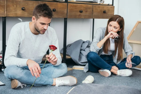 Sad woman and handsome man sitting on floor in robbed apartment — Stock Photo