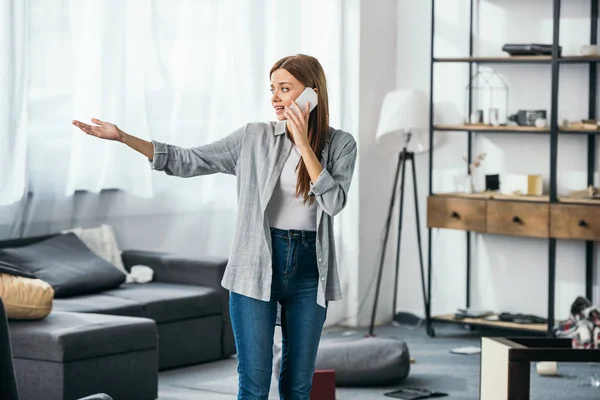 Attractive and sad woman talking on smartphone in robbed apartment — Stock Photo