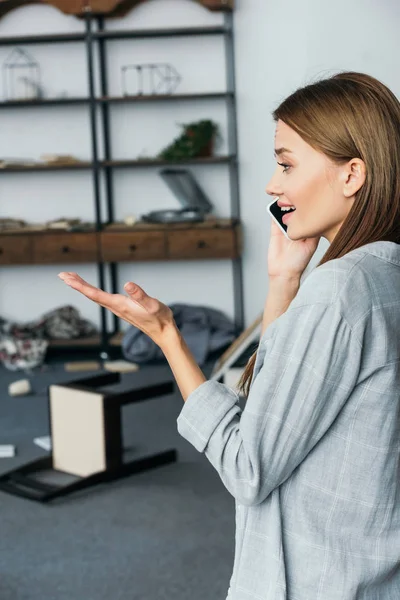 Side view of attractive and sad woman talking on smartphone in robbed apartment — Stock Photo