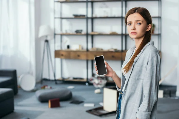 Mujer triste sosteniendo smartphone con pantalla en blanco en apartamento robado - foto de stock