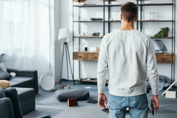 Back view of man in pullover looking at robbed apartment — Stock Photo