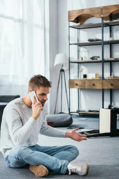 Handsome man talking on smartphone in robbed apartment — Stock Photo