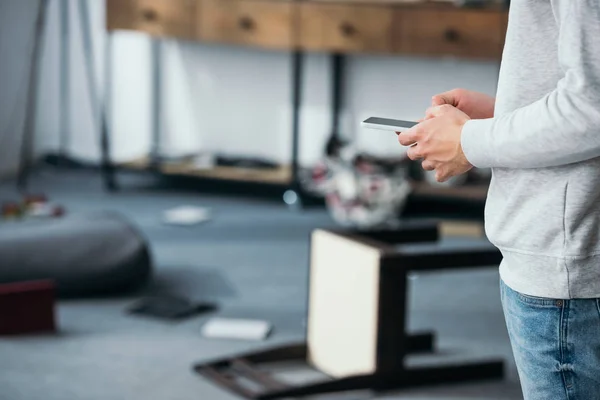 Cropped view of man using smartphone in robbed apartment — Stock Photo