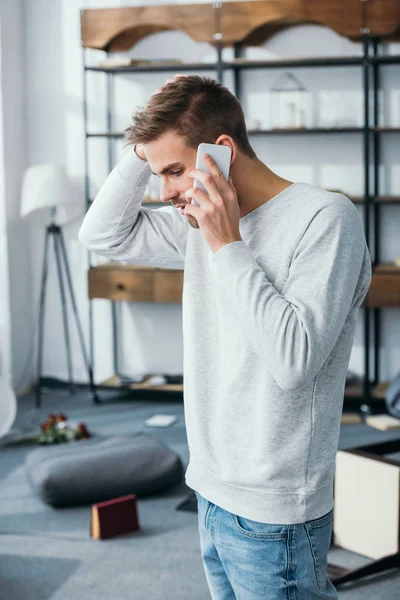 Seitenansicht eines gutaussehenden Mannes, der in beraubter Wohnung mit dem Smartphone spricht — Stockfoto