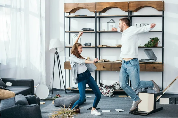 Lächelnde Frau und gutaussehender Mann mit ausgestreckten Händen tanzen in ausgeraubter Wohnung — Stockfoto