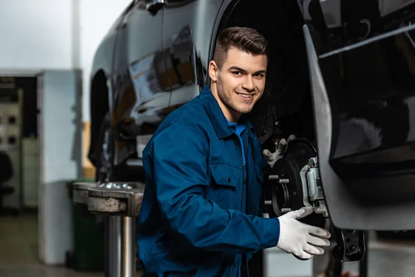 Young mechanic looking at camera while adjusting disc brakes — Stock Photo