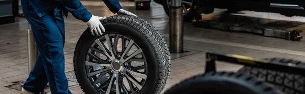 Cropped view of mechanic with car wheel in workshop, panoramic shot — Stock Photo