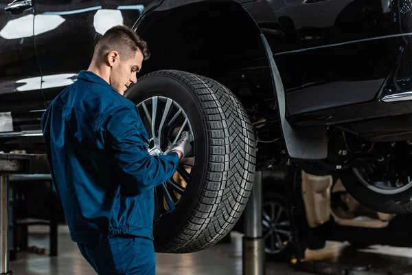 Jeune mécanicien installant la roue sur la voiture surélevée dans l'atelier — Photo de stock