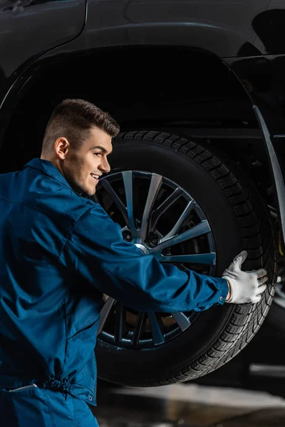 Un mécanicien souriant installant une roue sur une voiture surélevée en atelier — Photo de stock