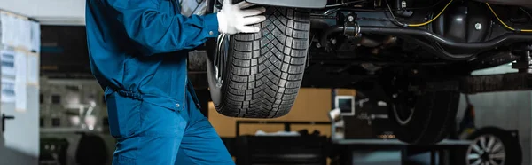 Cropped view of mechanic installing wheel on car in workshop, panoramic shot — Stock Photo