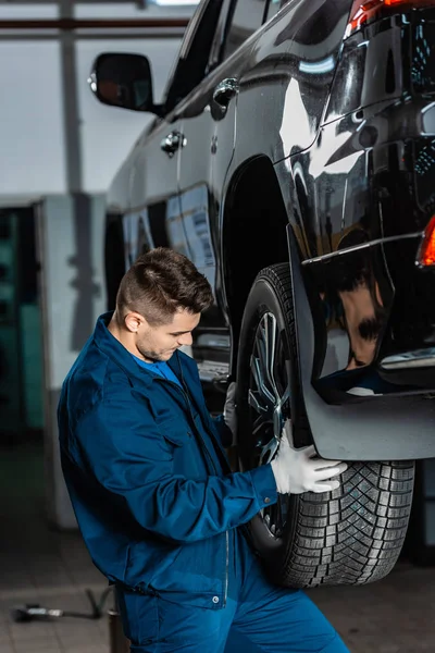 Jeune mécanicien installant la roue sur la voiture surélevée dans l'atelier — Photo de stock