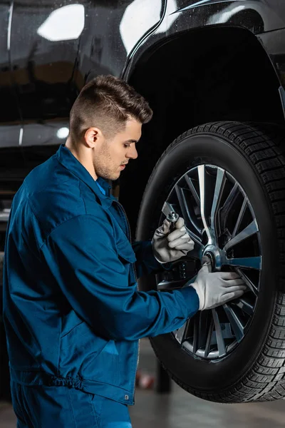 Mechanic looking at screw nut while fixing wheel on car — Stock Photo
