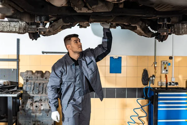 Attentive mechanic examining raised car in workshop — Stock Photo