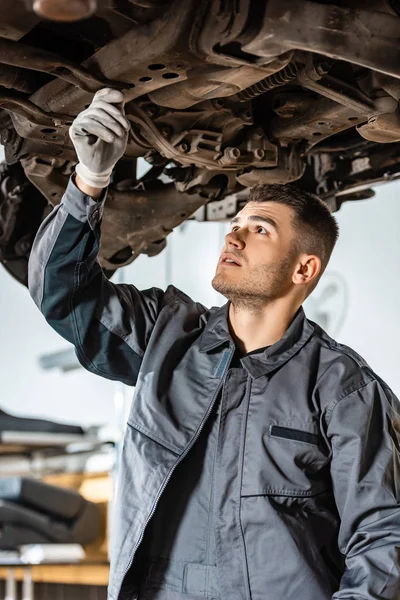 Attento meccanico esaminando auto sollevate in officina — Foto stock