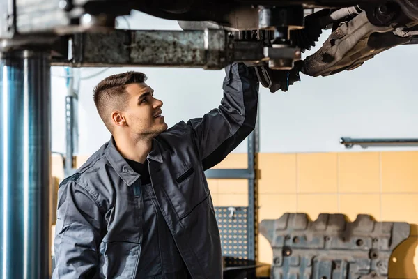 Young mechanic inspecting raised car in workshop — Stock Photo