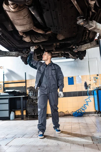 Young mechanic inspecting bottom of raised car in workshop — Stock Photo