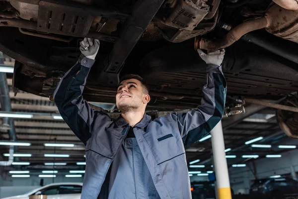 Lächelnder Mechaniker inspiziert Boden des Hochwagens mit Schraubenschlüssel — Stockfoto