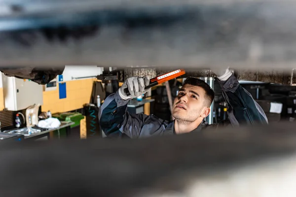 Selective focus of mechanic inspecting car bottom with flashlight — Stock Photo