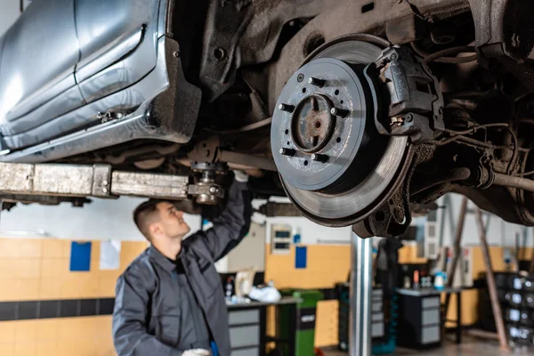 Selective focus of assembled disc brakes near young mechanic examining raised car — Stock Photo