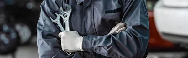 Cropped view of mechanic holding wrenches while standing with crossed arms — Stock Photo