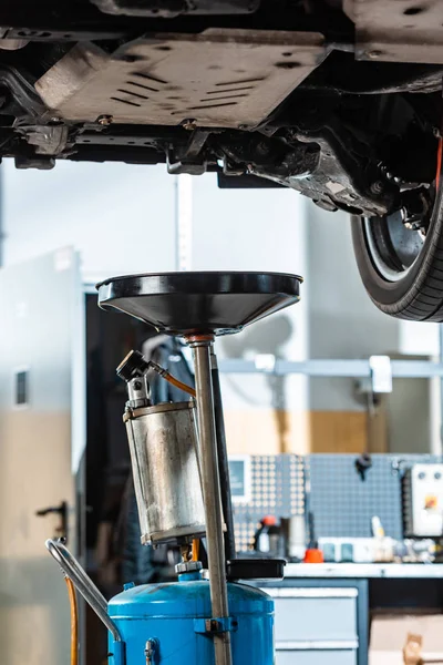 Pneumatic waste oil extractor under raised car in workshop — Stock Photo