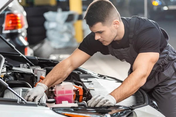 Giovane meccanico ispezionare vano motore auto in officina — Foto stock