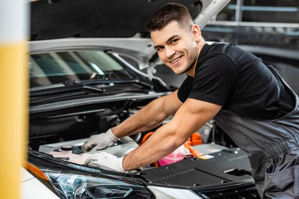 Selective focus of smiling mechanic inspecting car engine compartment — Stock Photo