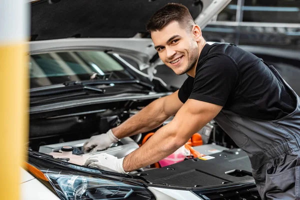 Foco selectivo del mecánico sonriente que inspecciona el compartimiento del motor del coche - foto de stock