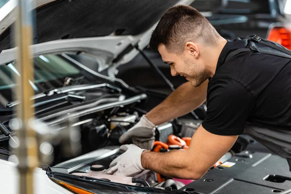 Selective focus of smiling mechanic inspecting car engine compartment — Stock Photo