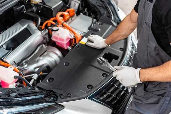 Partial view of mechanic holding wrench while inspecting car engine compartment — Stock Photo