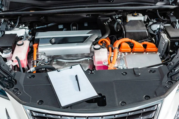 Portapapeles con papel blanco en blanco y bolígrafo cerca del compartimento del motor del coche - foto de stock