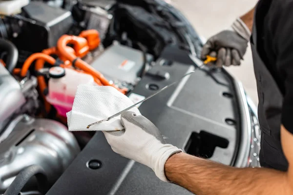 Vista recortada de la varilla de aceite de limpieza mecánica con trapo cerca del compartimento del motor del coche - foto de stock