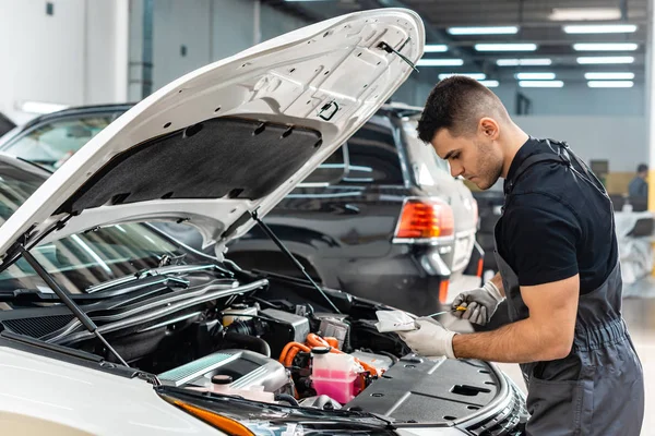 Pinza de aceite de limpieza mecánica joven con trapo cerca del compartimento del motor del coche - foto de stock