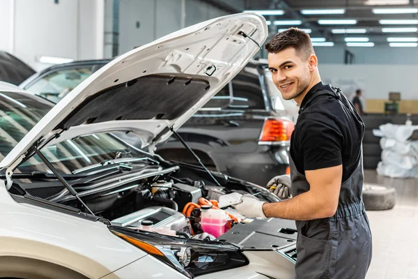 Schöner Mechaniker hält Ölmessstab in der Hand und lächelt in die Kamera — Stockfoto