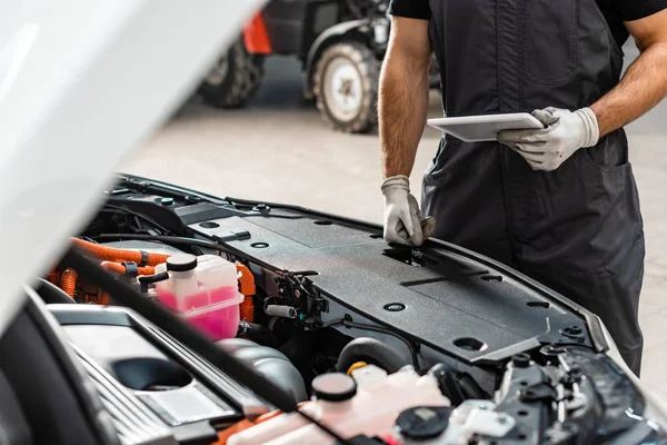 Vista parziale del meccanico che tiene tablet digitale vicino al vano motore dell'auto — Foto stock