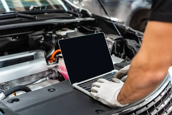 Vista recortada del mecánico utilizando el ordenador portátil cerca del compartimento del motor del coche - foto de stock