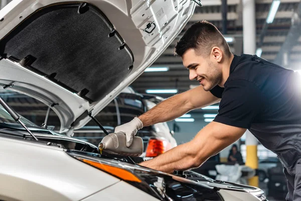 Mecánico sonriente verter aceite de motor en el motor del coche - foto de stock