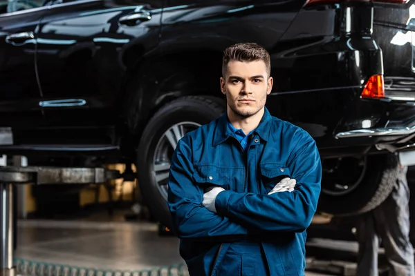 Handsome, serious mechanic standing with crossed arms and looking at camera — Stock Photo