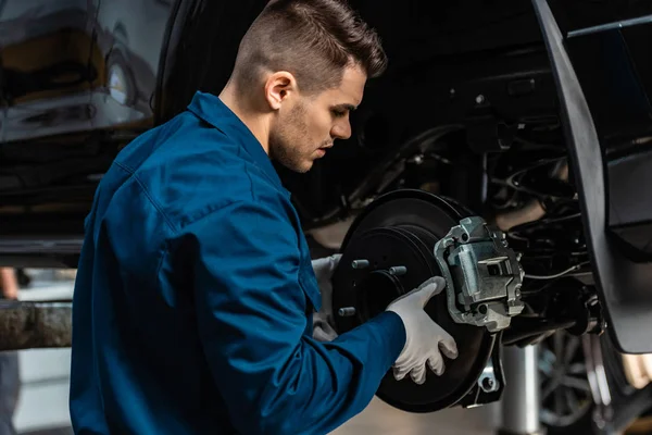 Joven, mecánico atento instalación de frenos de disco en el coche levantado - foto de stock