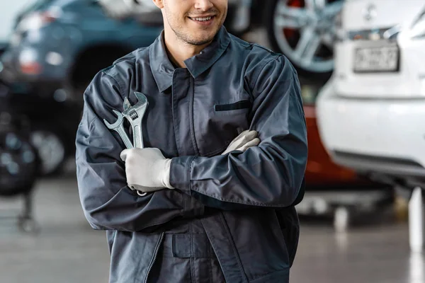 Cropped view of smiling mechanic standing with crossed arms and holding wrenches — Stock Photo