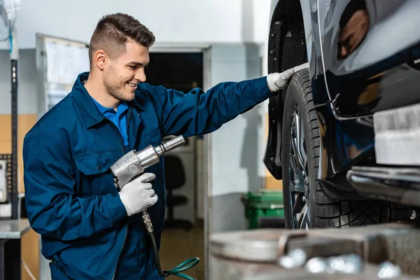 Selective focus of positive mechanic installing wheel on car with pneumatic wrench — Stock Photo