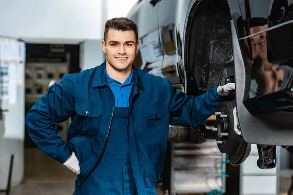 Smiling mechanic looking at camera while touching disc brakes of car — Stock Photo