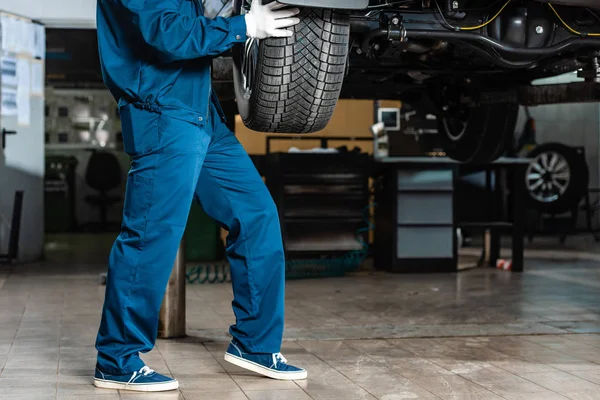 Vista ritagliata del meccanico installazione ruota su auto sollevata in officina — Foto stock