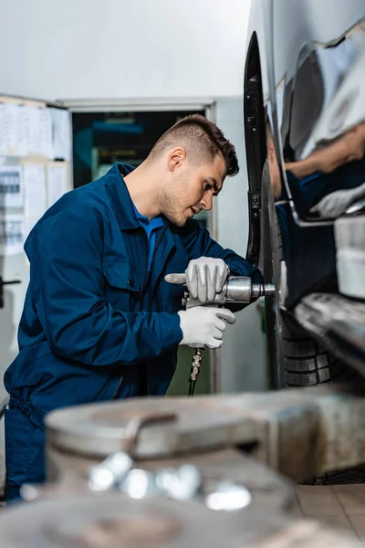 Selective focus of young mechanic installing wheel on car in workshop — Stock Photo