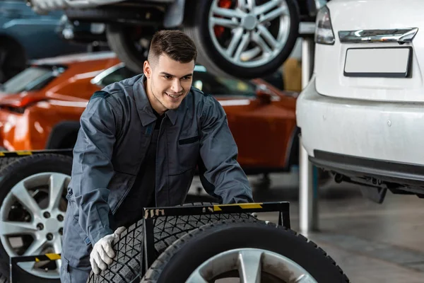 Schöner, lächelnder Mechaniker mit neuem Reifen in der Werkstatt — Stockfoto